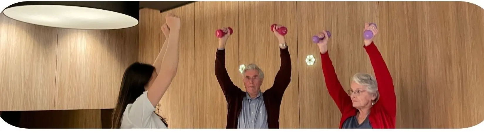 Three people standing with both arms raised, holding small dumbbells