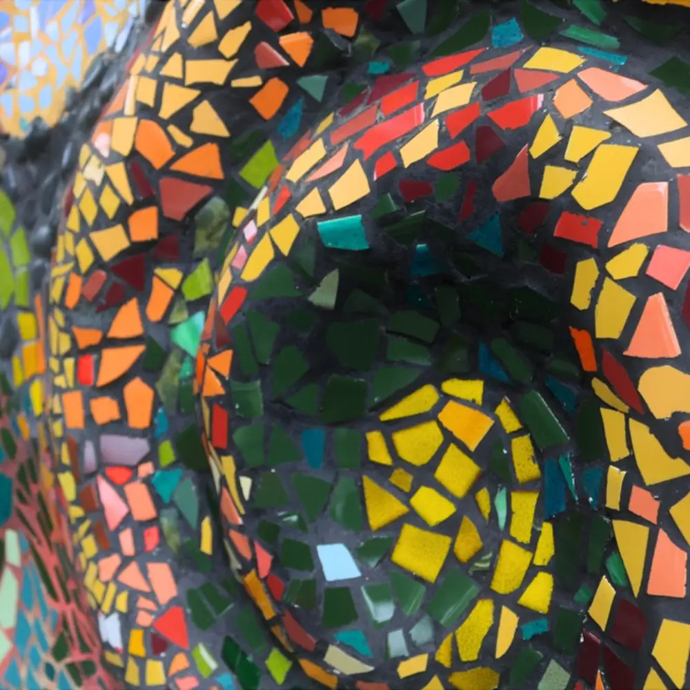 A close-up of the mosaic mural on the front wall: hundreds of small glass tiles in green, yellow, orange and red, laid in curving spirals