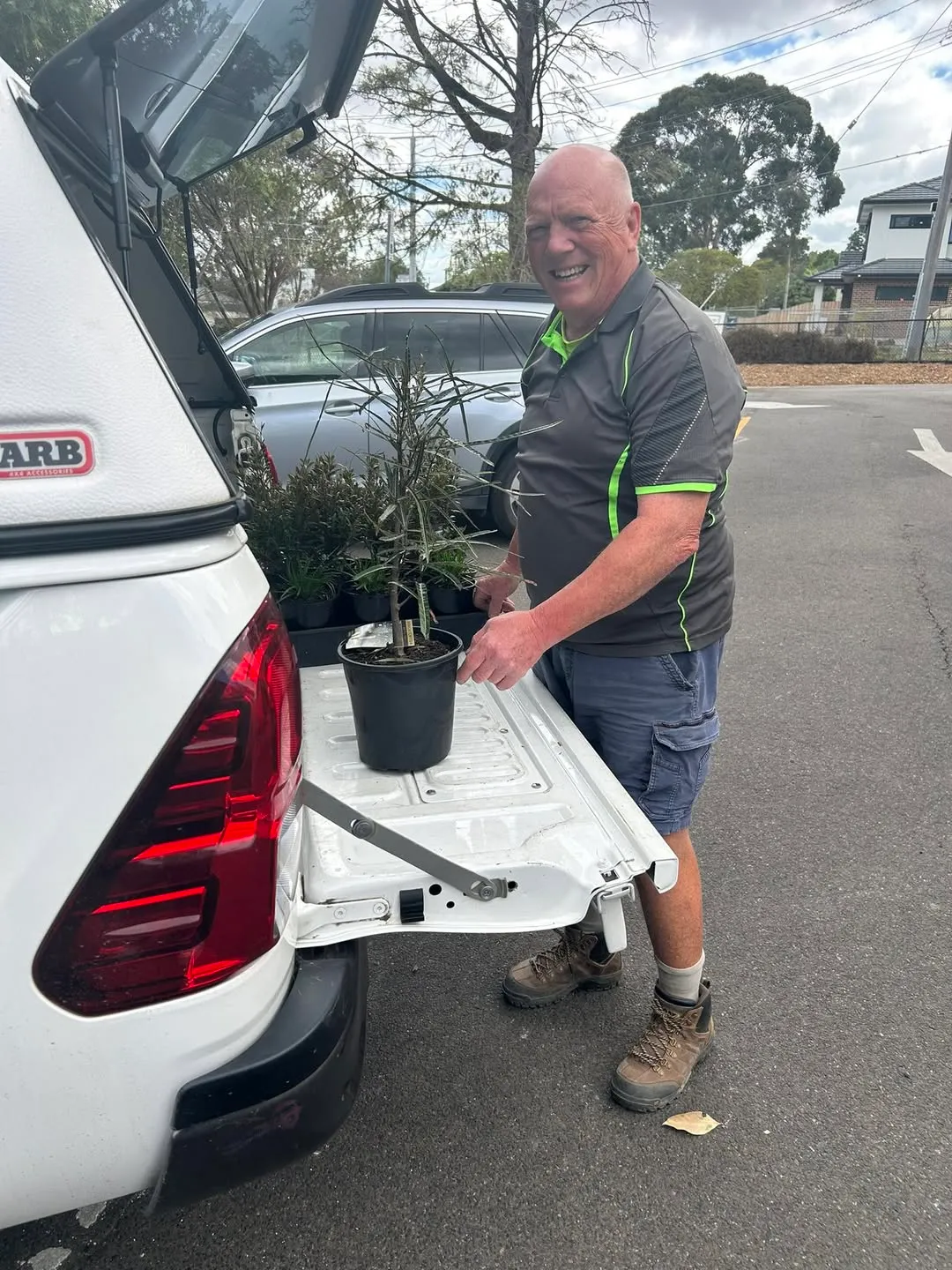 A landscaper unloading potted native plants from the back of a ute in the car park