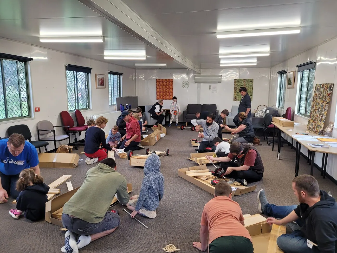 A room full of people of all ages building billy carts together on the floor